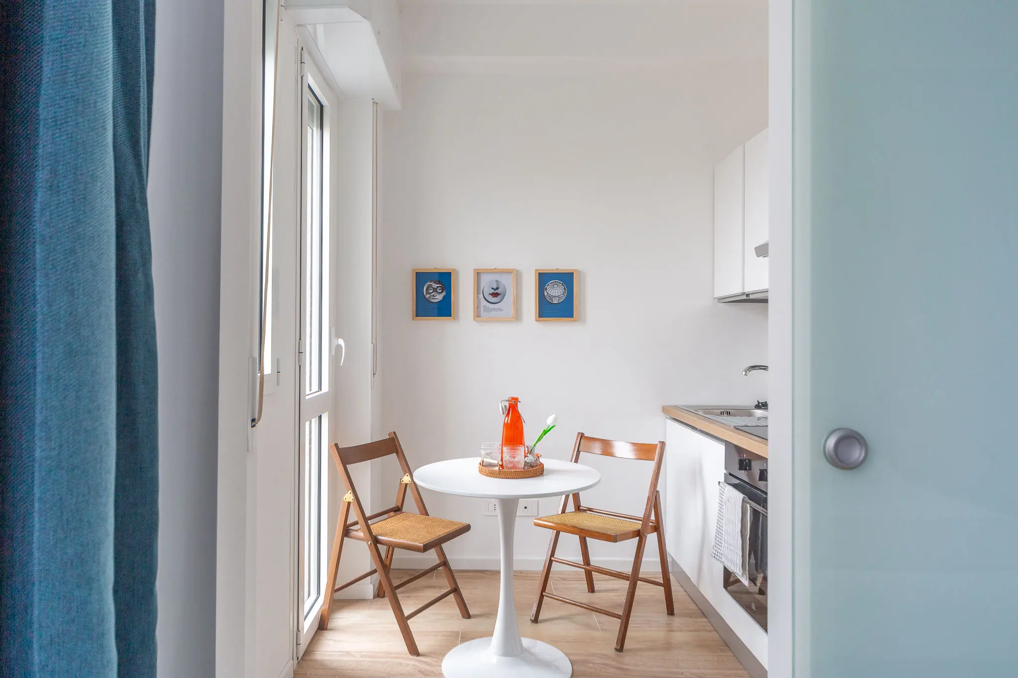 home-styling-di-cucina-con-il-tavolo-rotondo-e-sedie-vintage-in-fondo-quadretti-fornasetti